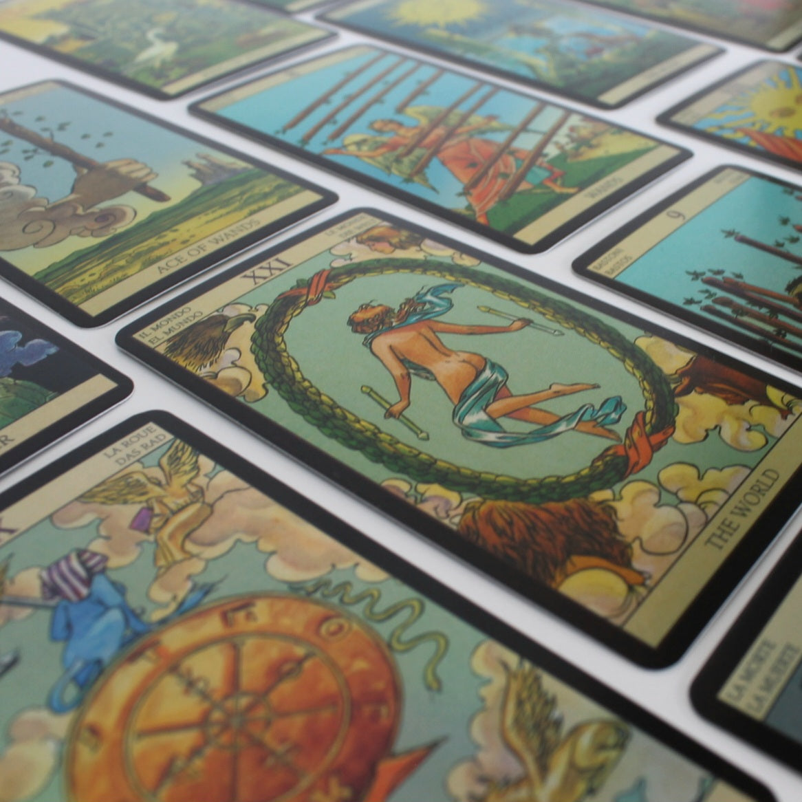 Różnobarwne karty tarota z symbolami, takimi jak słońce, gwiazdy i różne postacie, rozłożone w uporządkowany sposób na białym tle.