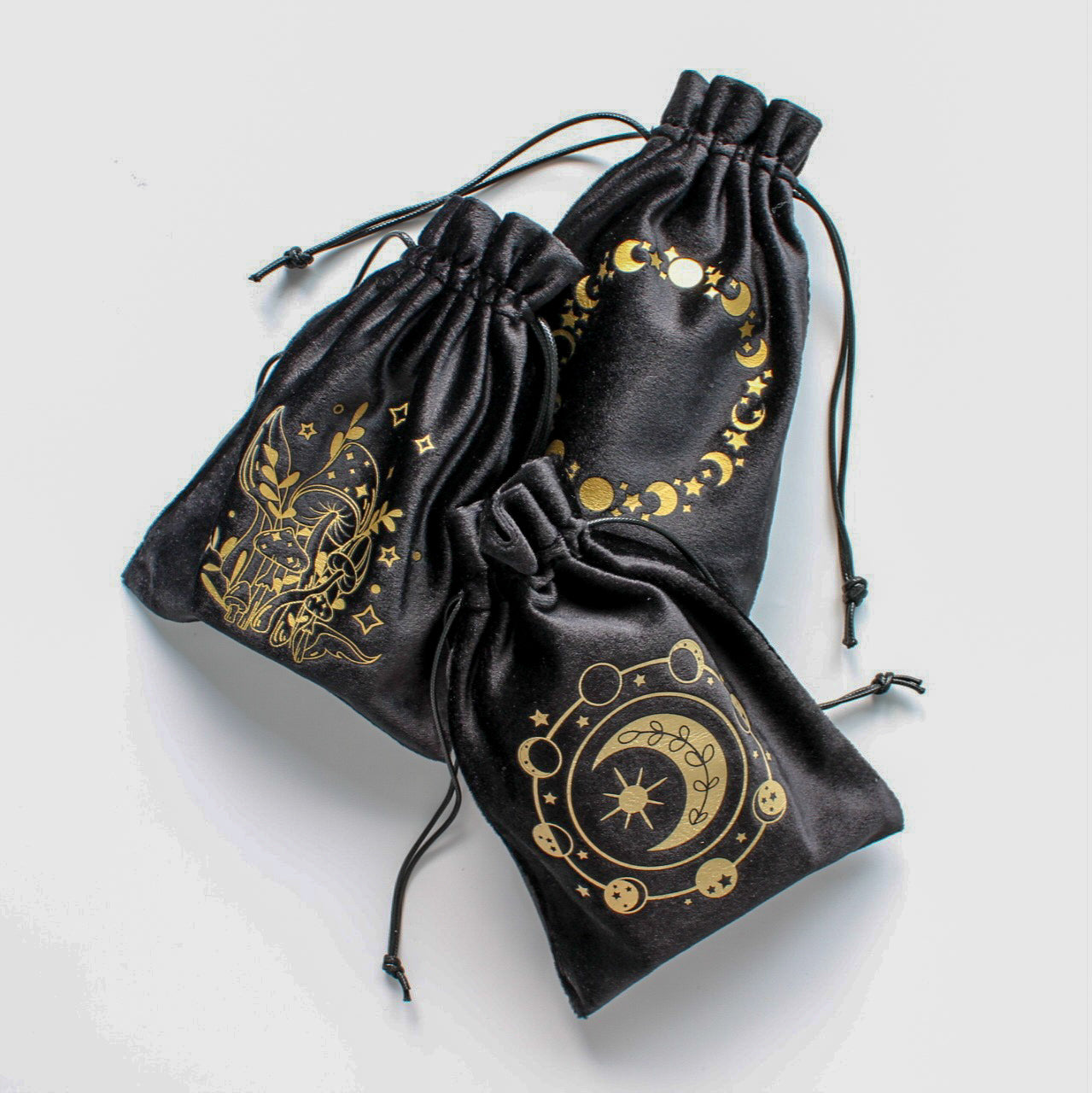 Kompozycja trzech woreczków ozdobionych złotymi symbolami inspirowanymi naturą i kosmosem, sfotografowana z góry na jasnym tle.