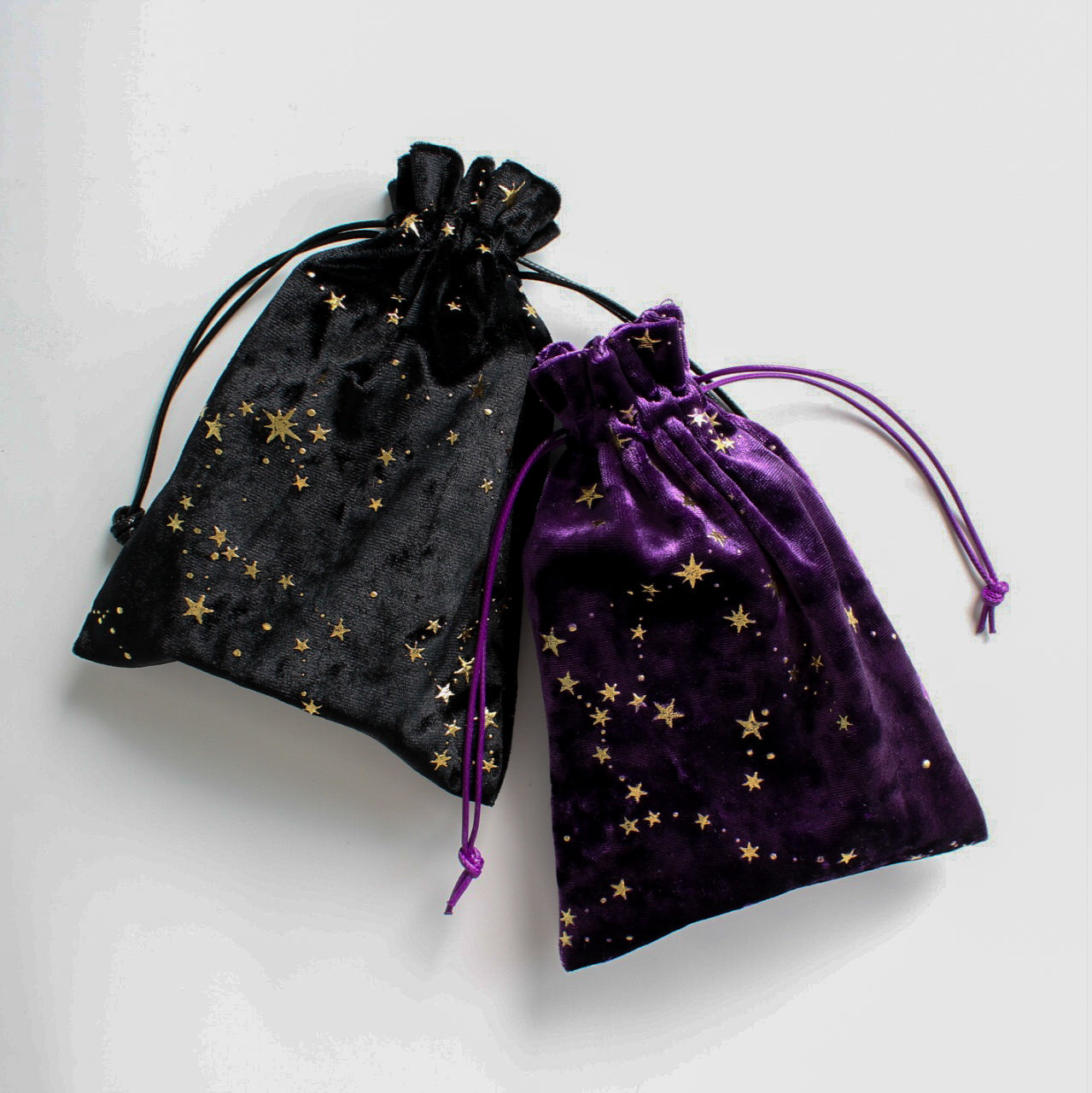 Dwa woreczki aksamitne – czarny i fioletowy – z motywem złotych gwiazd, ułożone obok siebie na jasnym tle.