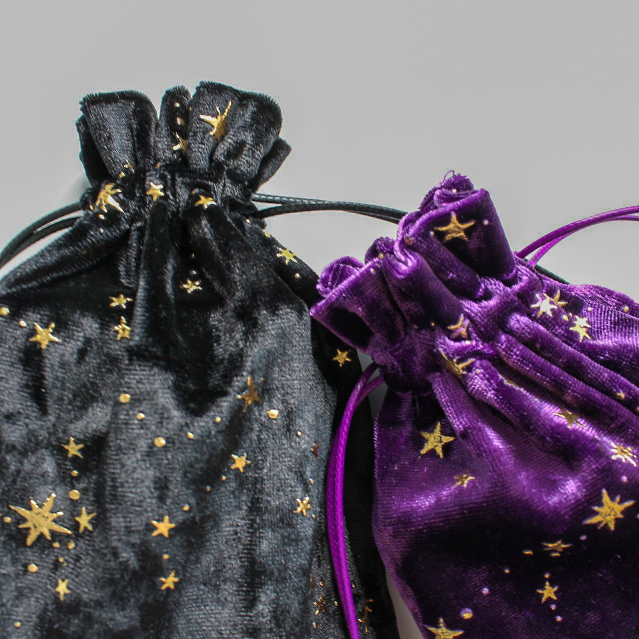 Zbliżenie na górne części czarnego i fioletowego woreczka, ozdobionych haftem złotych gwiazd, z widocznymi sznureczkami do zaciągania.