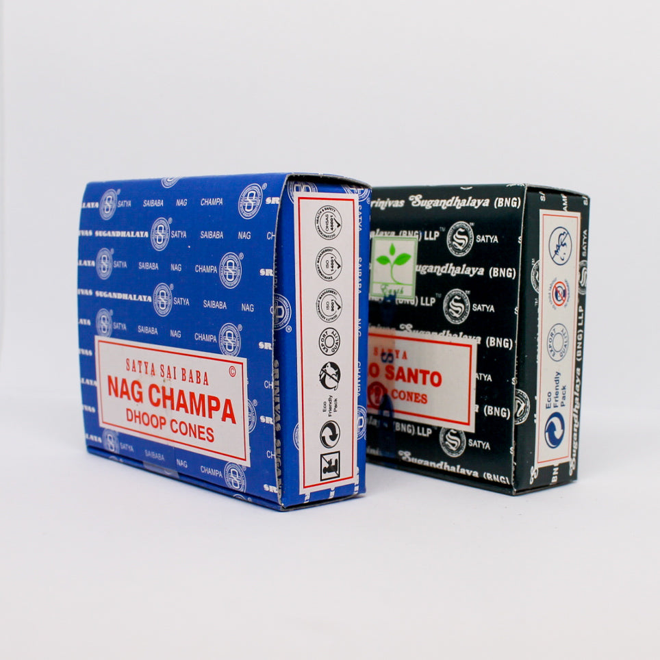 Zbliżenie na dwa pudełka kadzideł stożkowych: niebieskie Satya Nag Champa i czarne Satya Palo Santo. Widoczny jest bok opakowań z ikonami informującymi o cechach produktu, takich jak przyjazność dla środowiska.