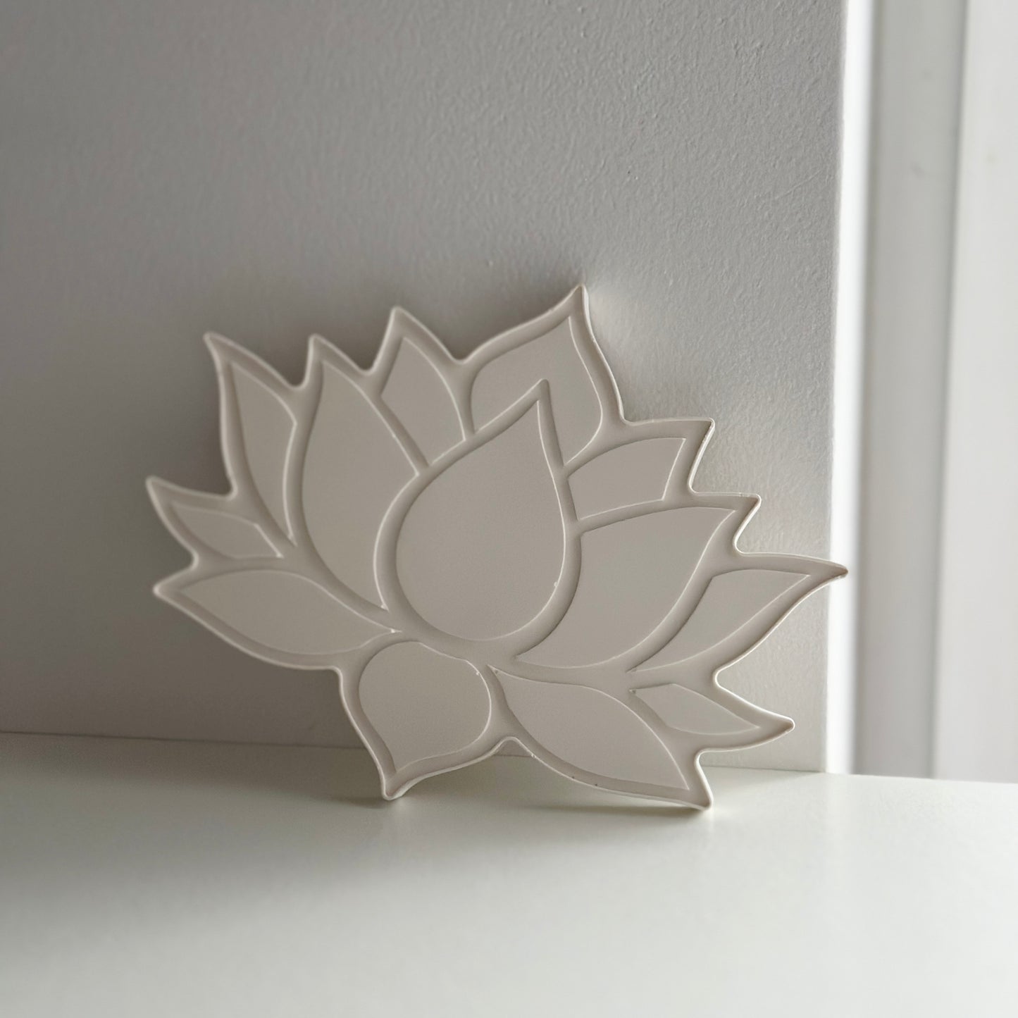 Ceramiczny stojak w kształcie kwiatu lotosu, w jednolitym jasnym odcieniu białym, o gładkiej i matowej fakturze.