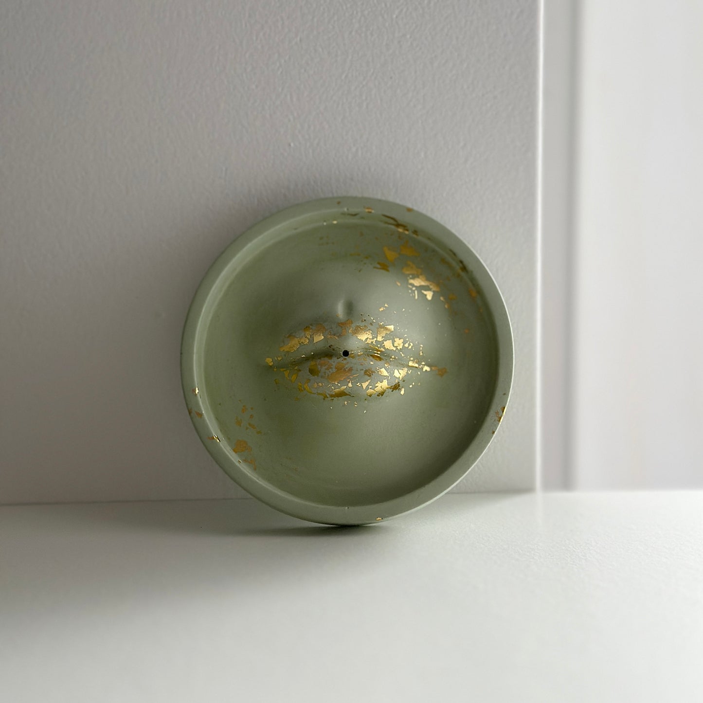 Okrągła podstawka w oliwkowym kolorze, zdobiona złotymi płatkami, tworzącymi nieregularny wzór na powierzchni.