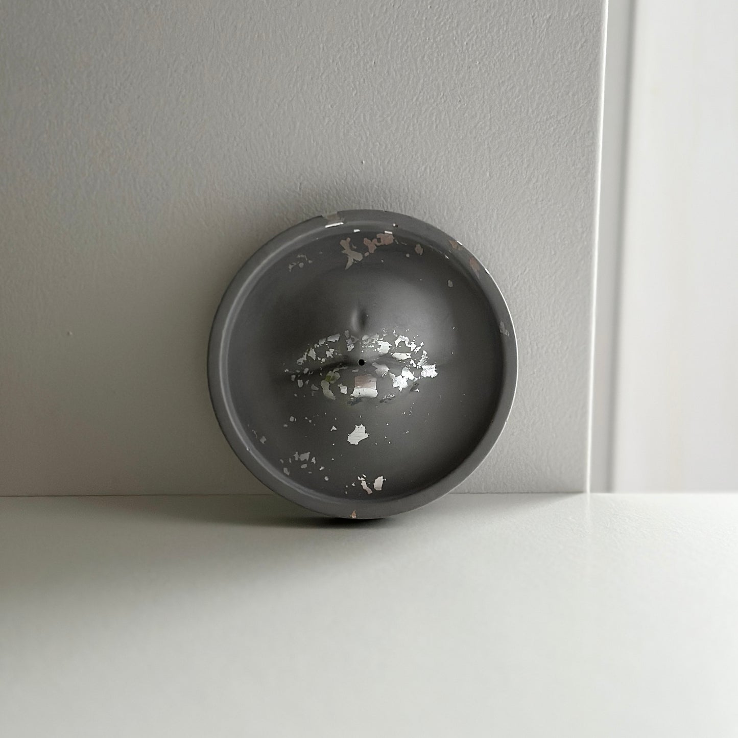 Szara, okrągła podstawka z delikatnym, błyszczącym wykończeniem oraz śladami zużycia, widoczne są drobne odpryski na powierzchni.