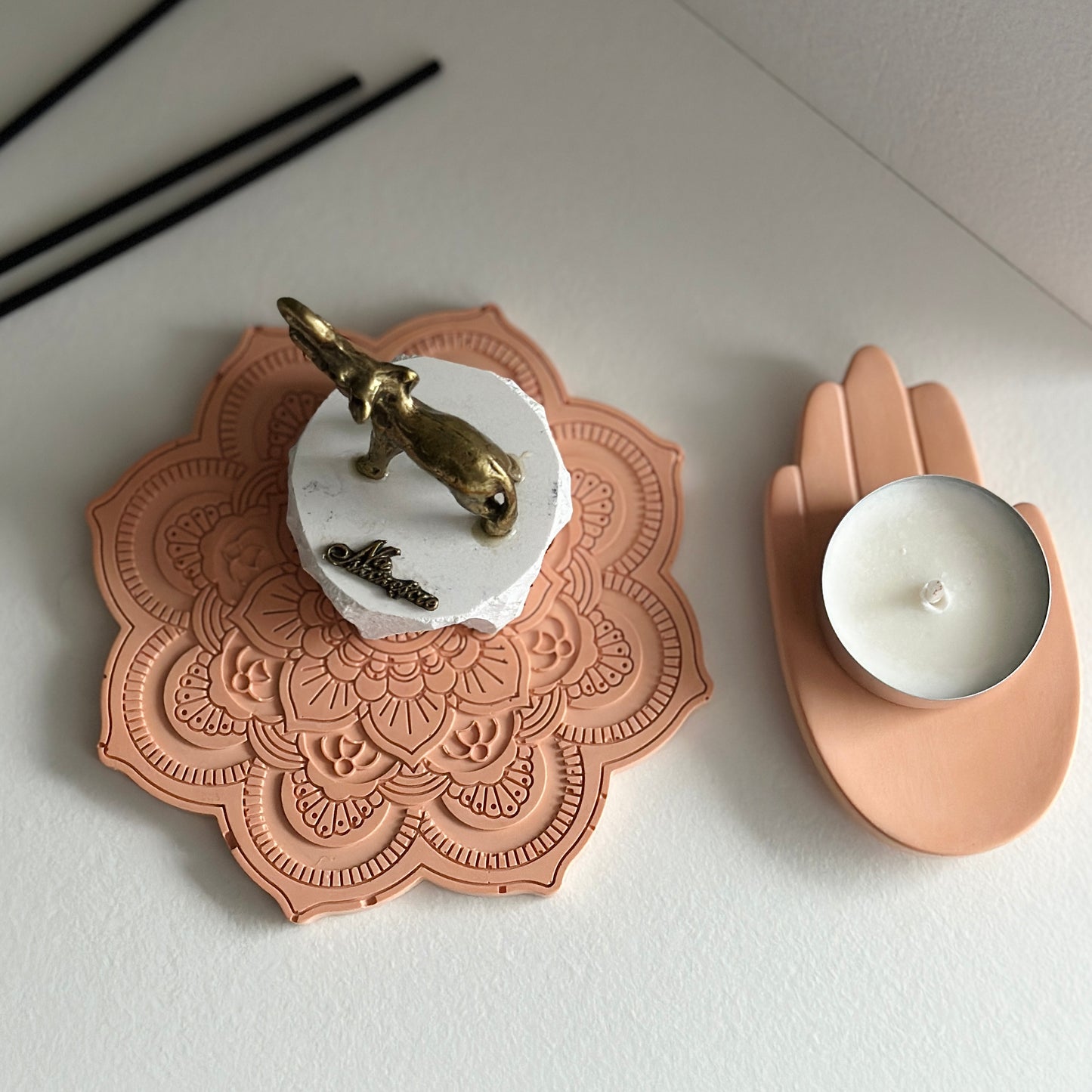 Zbliżenie na kompozycję: złota figurka słonia na mandalowej podstawce w kolorze beżowym, obok świecznik w kształcie dłoni. Całość w minimalistycznym, eleganckim stylu.