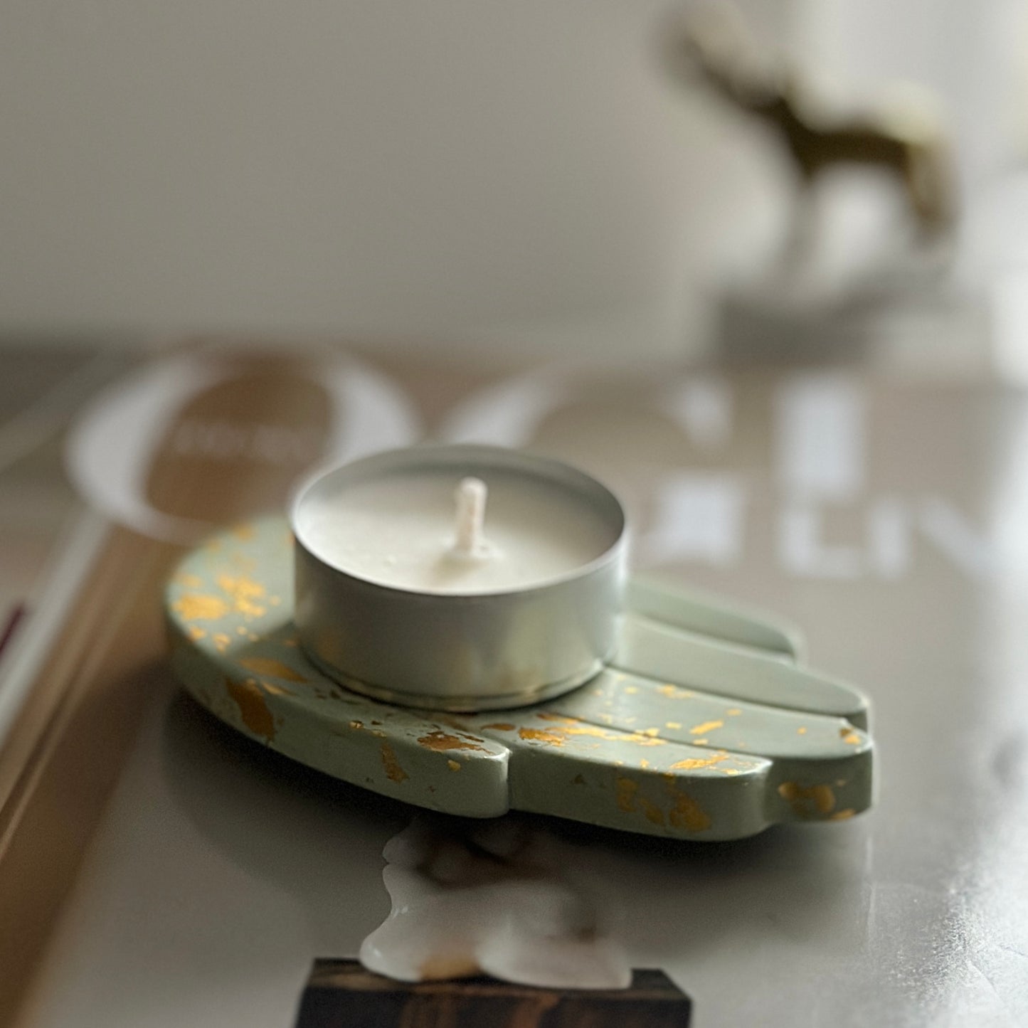 Zielony świecznik w kształcie dłoni, ozdobiony złotymi plamkami, stoi na okładce magazynu "Vogue", w tle widoczna złota figurka słonia.