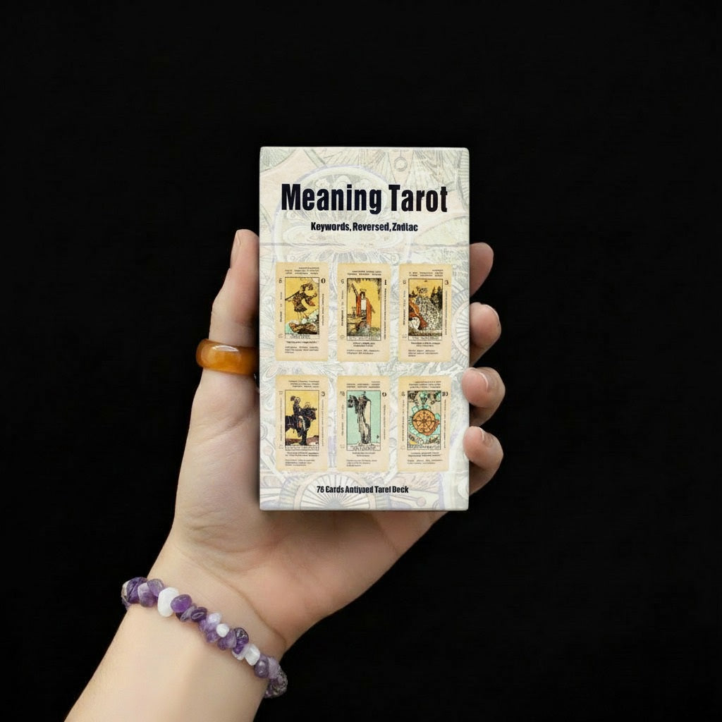 Dłoń trzymająca pudełko talii kart "Meaning Tarot" z sześcioma kartami tarota w stylu vintage na okładce, osoba ma na nadgarstku bransoletę z fioletowych i białych kamieni.