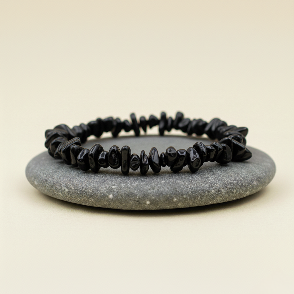 Bransoletka z nieregularnych czarnych kamieni, ułożona na szarym kamieniu na beżowym tle.