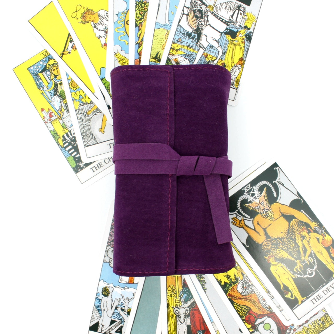 Fioletowy aksamitny futerał na karty tarota przewiązany wstążką, otoczony kolorowymi kartami tarota
