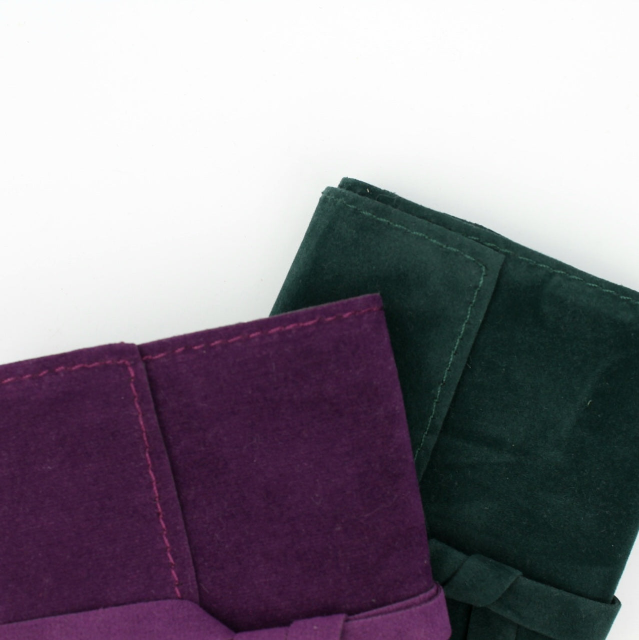Zbliżenie na detale dwóch aksamitnych woreczków - fioletowego i ciemnozielonego - pokazujące teksturę materiału i szwy