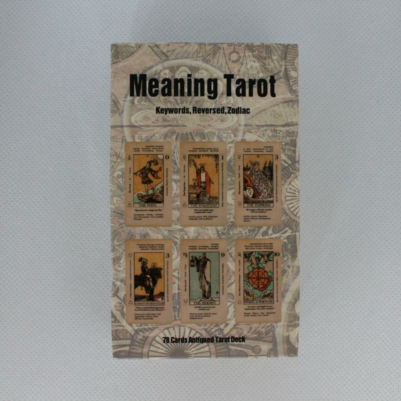 Zdjęcie przedstawia opakowanie talii kart tarota zatytułowanej "Meaning Tarot" z grafiką przedstawiającą sześć kart na przodzie pudełka. Na pudełku znajdują się także słowa kluczowe: "Keywords, Reversed, Zodiac". Talia składa się z 78 kart o antycznym wyglądzie.